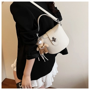 Detail of cream-colored pebble leather underarm bag with silver lock and bear charm