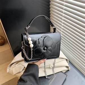 Detail of a black leather handbag with a large 3D flower and a pearl chain strap