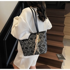 Detail of black geometric pattern tote bag featuring a decorative pink woven tassel charm