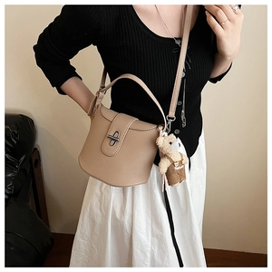 Detail of beige bucket bag with metal lock, top handle, and cute plush bear charm