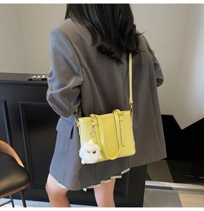 Close-up of lime green bucket bag featuring a white plush monster charm and shoulder strap