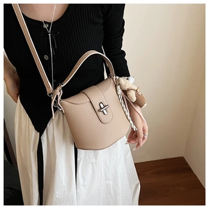 Chic beige bucket bag with metal lock and cute bear charm shown on model in a soft room