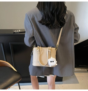 Detail of beige bucket bag with gold buckle and a cute fuzzy eye charm on side strap