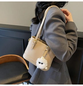 Detail view of a beige leather bucket bag with a cute plush monster charm and strap