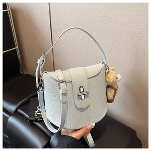 Detail of mint green lychee pattern leather handbag with silver rotary buckle and bear charm