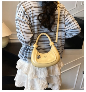 Close-up of yellow crescent bag with leather texture and metal pendant worn by a model
