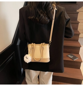 Detail of a two-tone bucket bag with plush pompom on a wooden staircase