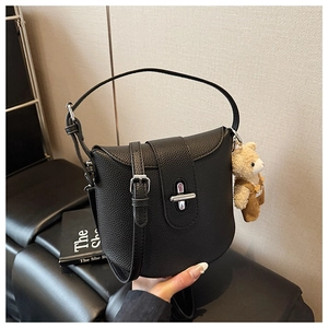 Detail of black pebbled leather bucket bag with silver turn-lock and cute bear charm
