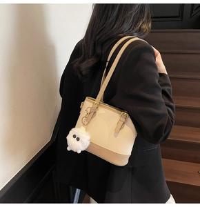 Detail of a cream and light brown bucket bag featuring gold hardware and a plush charm
