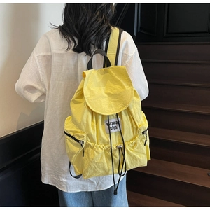 Detail view of the drawstring opening and flap closure on a bright yellow nylon backpack