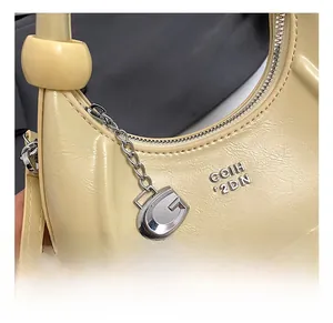 Detail shot of the beige litchi leather moon bag featuring a silver metal G pendant