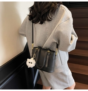 Detail view of a black leather bucket bag with a cute white plush pendant charm