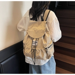 Close-up of a beige nylon backpack featuring a drawstring closure and a woven logo label