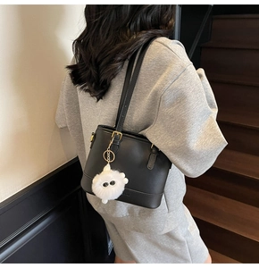 Rear view of a minimalist black bucket bag with a white plush doll charm accessory