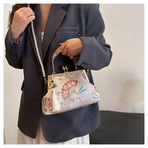 Detail of vintage shell bag with gold handle, floral embroidery, and pearl strap