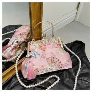 Detail of pink embroidered silk bag with pearl chain and tassel on reflective surface