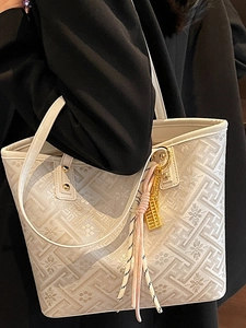 White casual tote bag with geometric floral patterns and tassel charm shown on shoulder