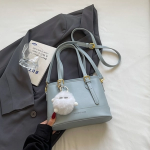 Detailed top view of Morandi blue-grey bucket bag with plush charm on a grey blazer background