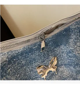 Close-up of silver butterfly charm and metal zipper on blue denim fabric tote bag