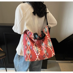 Detail of red canvas tote bag with ethnic patterns and black woven strap on a model