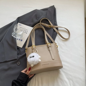 Close-up of beige bucket bag with gold hardware and a soft white pom pom keychain