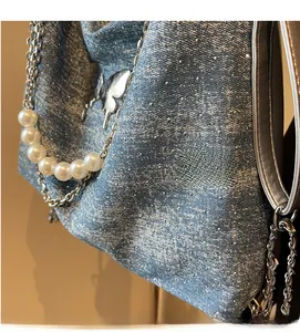 Detail of light blue washed denim tote featuring pearl charms and silver butterfly charm