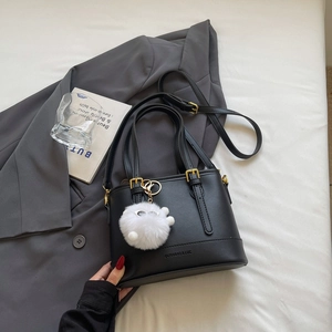 Detail view of a black bucket bag with a golden buckle and a white plush ball charm