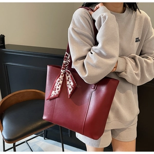 Detail einer weinroten Leder-Tote-Bag mit elegantem Seidenschal und goldener Beschriftung