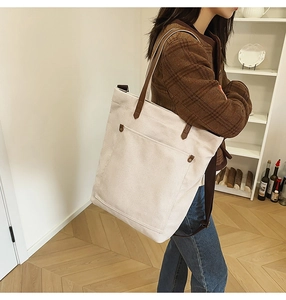 Detail view of canvas tote bag with brown leather strap and metal buckle pocket