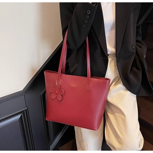 Rote Damen-Einkaufstasche mit Logo und Blumenanhänger, getragen von einem Modell