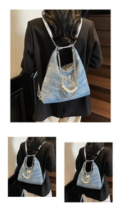 Detailed view of blue denim backpack with silver butterfly charm and pearl chain accent