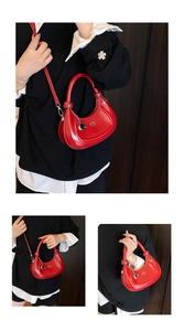 Detail of red crescent bag with gloss finish, brand lettering, and metal chain accent