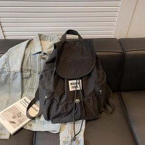 Detail of nylon backpack with drawstring closure and white logo tag on black leather couch