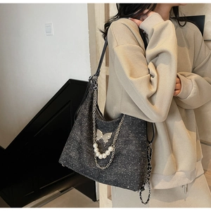 Detail of black tote bag with silver butterfly charm and white pearl chain strap