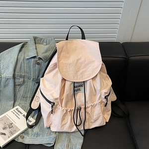 Detail of light pink nylon drawstring backpack on sofa with denim jacket and book