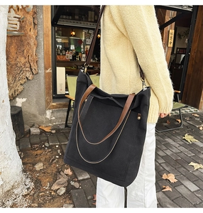 Detail view of black canvas tote bag with brown leather handles and side zipper accents