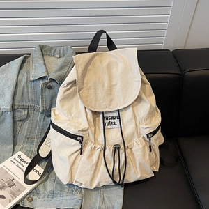 Detailed view of cream nylon drawstring backpack with black label and side zipper pockets