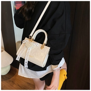 Detail van witte getextureerde mini crossbodytas met parelboog en geweven handvat