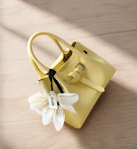 Detail der hellgelben Krokodilmuster-Eimertasche mit großem weißem Blumenanhänger