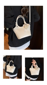 Detail of cream white glossy bucket bag featuring pearl bow and lace charm decoration