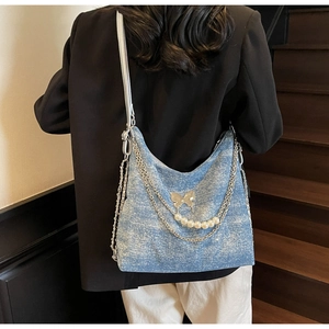 Detail of light blue textured tote bag featuring a silver butterfly buckle and pearl chain