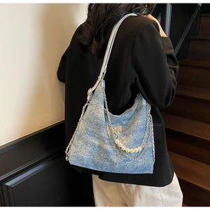 Detail of denim tote bag with silver butterfly buckle, pearl charms, and metallic chains