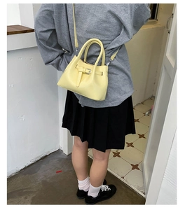 Detailansicht einer hellgelben Kunstlederhandtasche mit Gürtelschnalle und Trageriemen