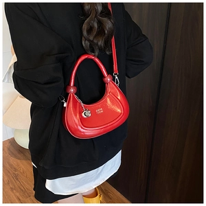 Detailed view of glossy red crescent bag with metallic C-shaped charm and logo text