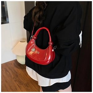Close-up of bright red patent leather crescent bag with gold logo and silver metal pendant
