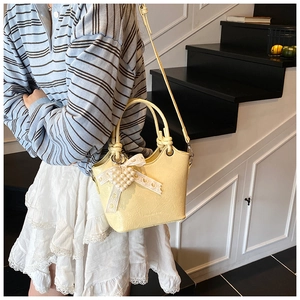 Detail of pale yellow bucket bag with lace bow and pearl heart charm on leather texture