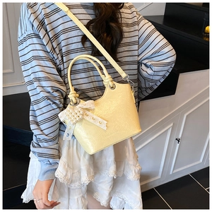Detail view of yellow bucket bag with metal ring handle and pearl lace bow on a model