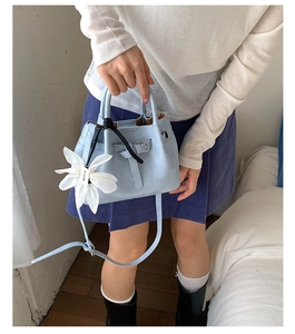 Detail der hellblauen Handtasche aus Leder mit Krokoprägung und Blumenanhänger