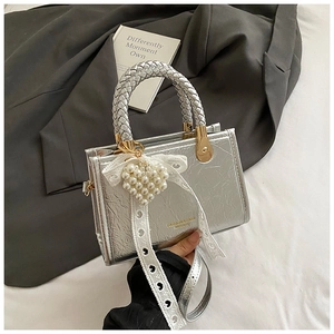 Detail van zilveren metallic handtas met parelhart hanger en kanten strik decoratie