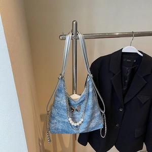 Detail of blue denim tote bag with silver chain, butterfly charm, and pearl strap decoration